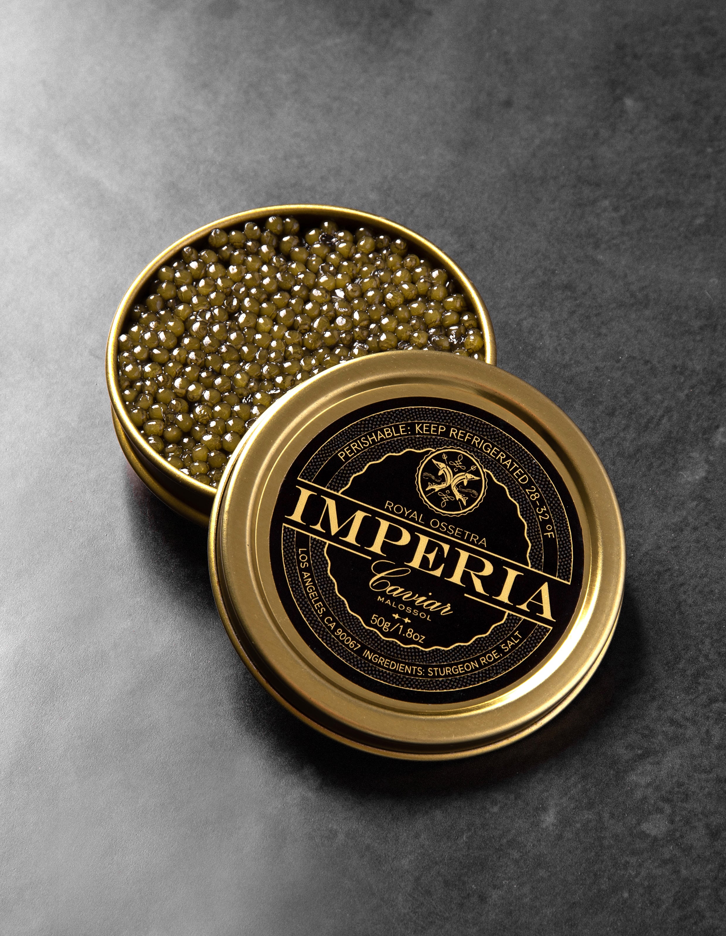 Open 50g tin of Imperia Royal Ossetra Caviar showing golden-green pearls with the branded black and gold lid on a dark slate surface.