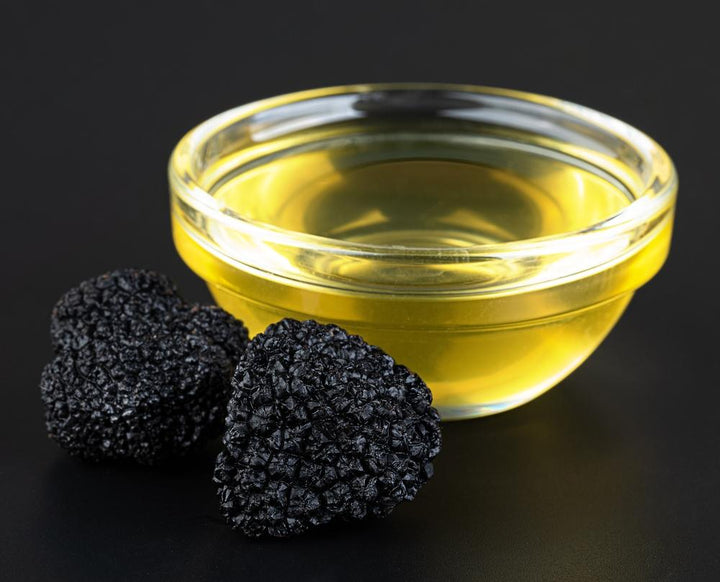 Two black truffles in front of a golden dish of premium truffle oil
