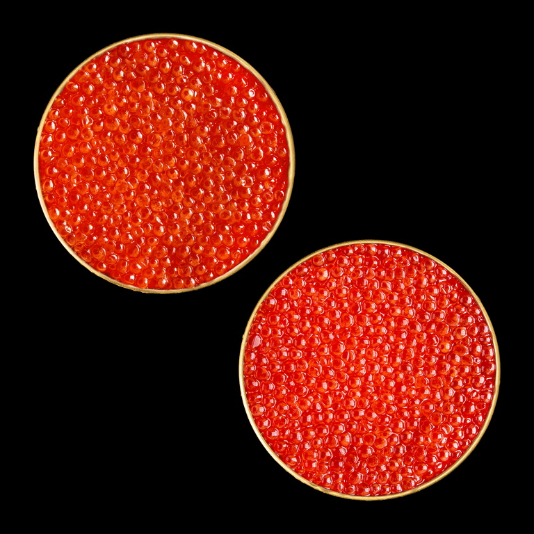 Top-down view of two open tins of bright orange-red smoked trout roe and wild Alaska salmon roe on a black background.