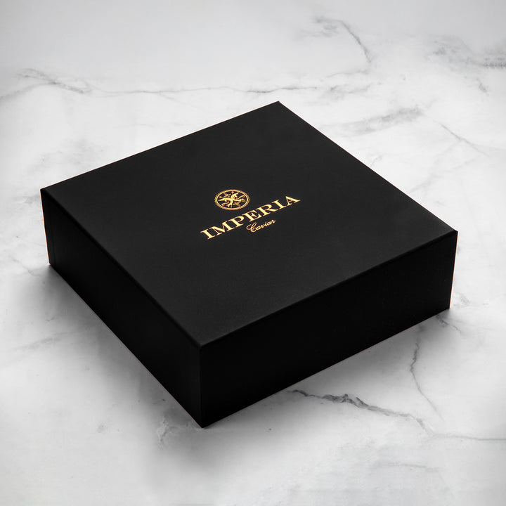 Closed Imperia Caviar matte black gift box with gold foil logo on a marble surface.