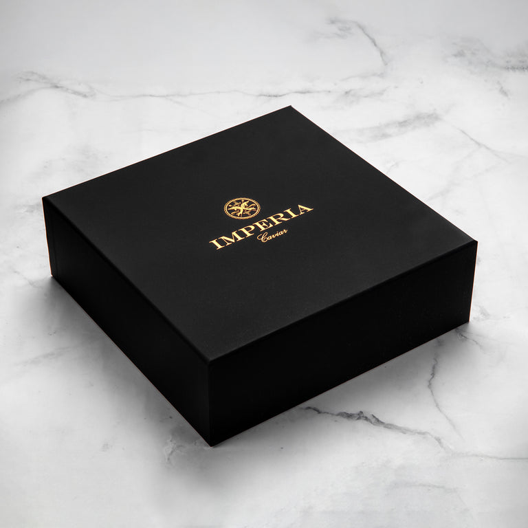 Closed Imperia Caviar matte black gift box with gold foil logo on a marble surface.