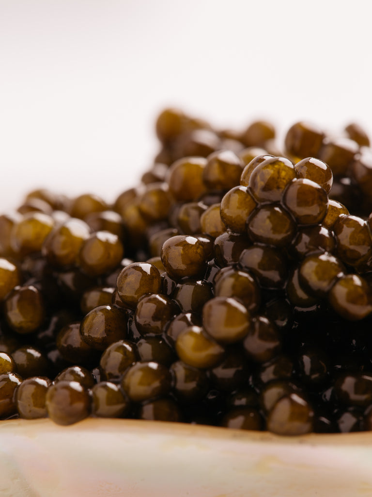 Extreme close-up of Imperia Amur caviar pearls showing glossy, dark olive-brown beads on a mother of pearl spoon.