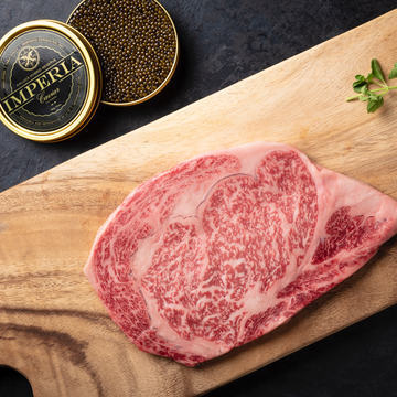 A piece of Wagyu beef on a wooden cutting board, with a tin of caviar and a small container of truffle salt in the background.
